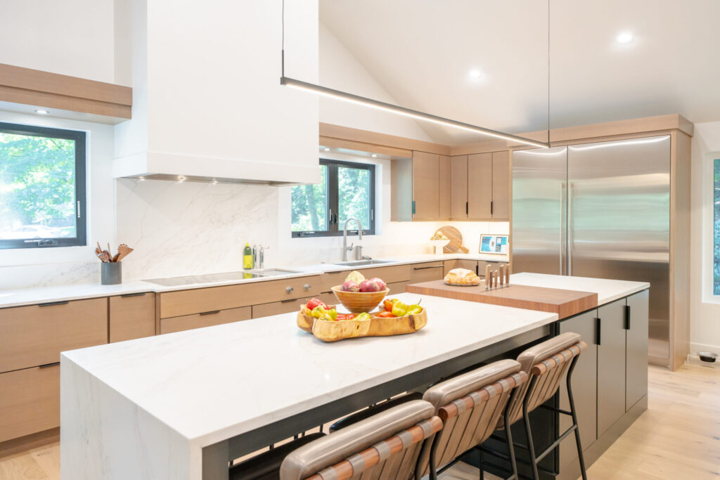 Kitchen with light wood cabinets, a white waterfall island, seating for three, and a built-in butcher-block prep surface.